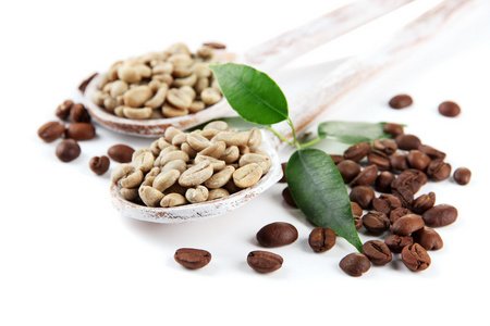 绿色和棕色咖啡豆的木质勺子和叶子上白色隔离