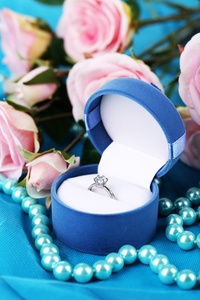 玫瑰和蓝色布上的订婚戒指