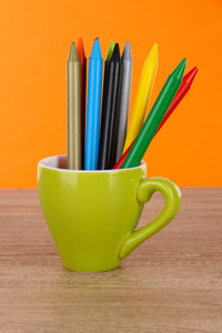 彩色铅笔在橙色背景上桌上的杯子