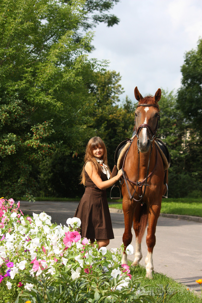 美丽的女孩在床边的花的连衣裙和马肖像