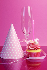 粉红色生日蛋糕用圆点蜡烛粉红色背景下，与党的帽子和香槟玻璃与粉色圆点丝带