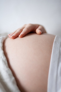 怀孕的女人抱着她的肚子，用她的手
