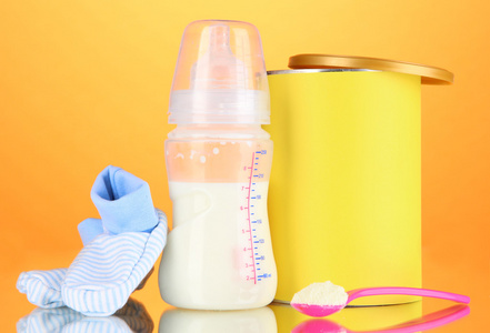 与牛奶和橙色背景上的婴儿食品瓶