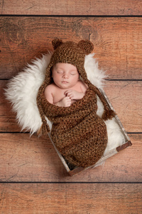 戴着棕色钩的熊帽子和睡在一个老式的木制框名初生男婴