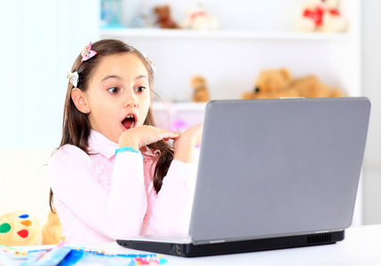 可爱的小女孩微笑着和看着笔记本电脑，使用的便携式计算机的小女孩