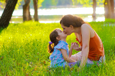女儿妈妈亲吻宝宝女人坐在绿色的草地上