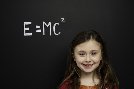 聪明的年轻女孩站在面前的一块黑板