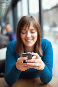 年轻美丽的女孩在一家咖啡馆中使用智能手机