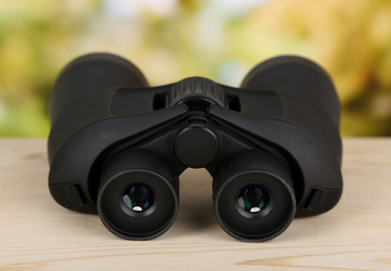 在绿色背景上的木桌上的黑色现代双筒望远镜