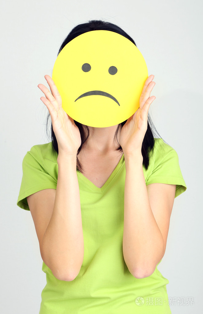 年轻女子持纸与悲伤的笑脸灰色背景