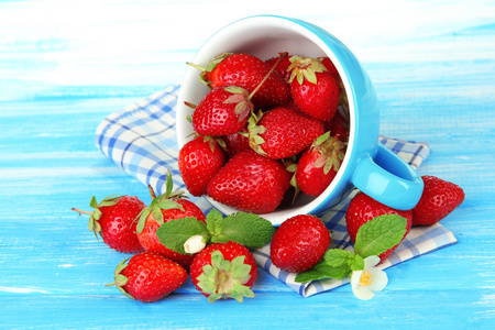 成熟的甜草莓在蓝色的木桌上的杯子