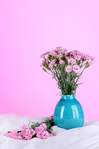 在粉红色的背景上的白色织物上的花瓶里的许多小粉红丁香