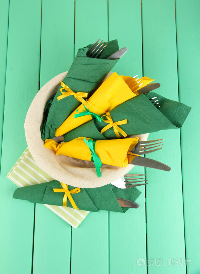 裹着绿色和黄色纸餐巾彩色木制背景上的刀子和叉子