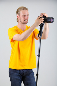 帅气摄影师用相机上脚架，灰色背景