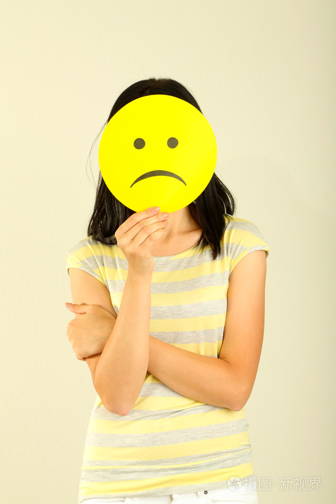 年轻女子持纸与悲伤的笑脸灰色背景