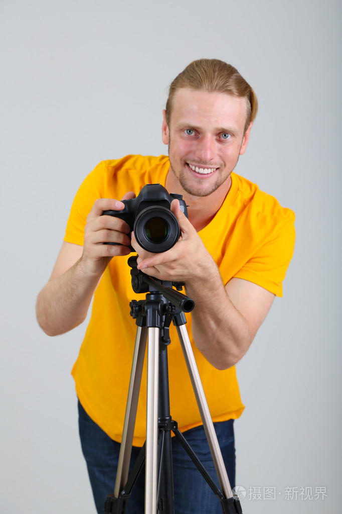 帅气摄影师用相机三脚架灰色背景上