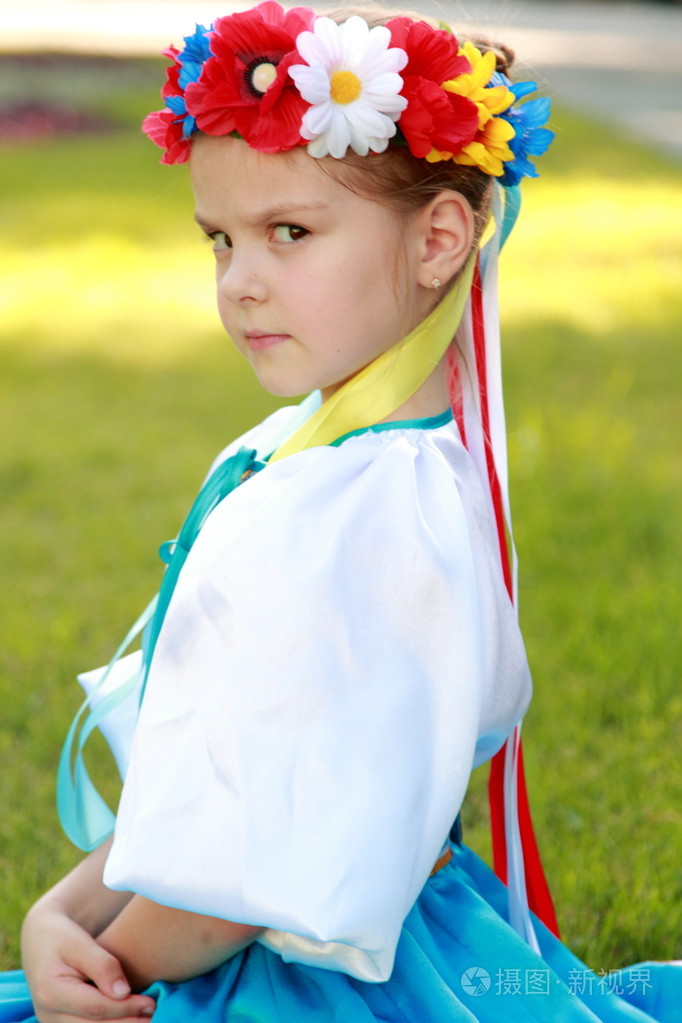 在美丽的民族服装的迷人微笑的可爱小女孩乌克兰是在背景上的绿草户外