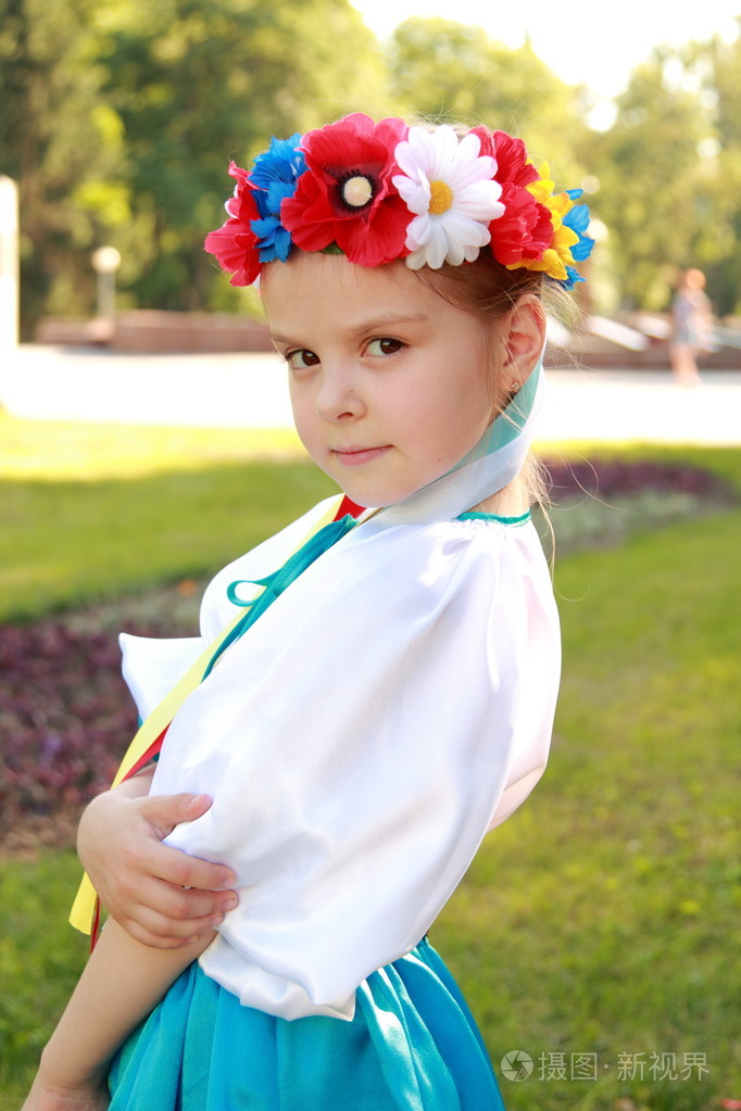 微笑小女孩在鲜艳的民族服装,乌克兰是在背景上的绿草中夏公园