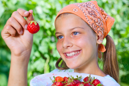 漂亮的小微笑女孩在花园里吃草莓
