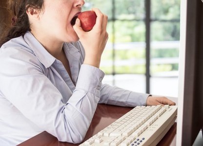 在计算机上工作和吃苹果红的女人