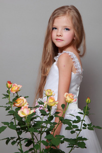 持有与灰色的背景上的绿色叶子黄玫瑰的美丽健康长头发的白种人女孩