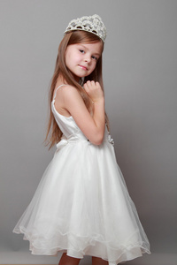 皇冠和可爱的笑容摆在灰色的背景上的摄像头白色连衣裙的美丽头发的白种人小女孩