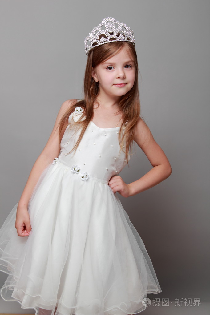 欧洲可爱的年轻女孩,戴着一顶王冠和可爱的笑容在假期白色连衣裙