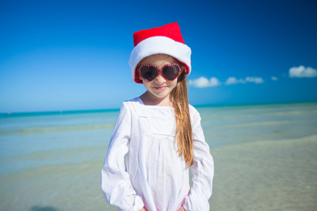 穿红衣的小女孩帽子圣诞老人和太阳镜在异国风情的海滩上