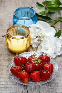 草莓 蜡烛和木桌上的白牡丹花卉