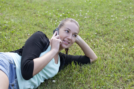 年轻女子躺在草地上，用手机在手