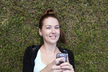 年轻女子躺在草地上，用手机在手