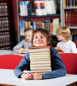 小学生休息的书在图书馆中的表堆栈上的下巴