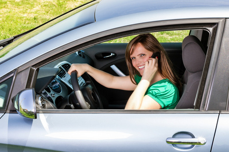 微笑着的年轻女子开车时使用智能手机