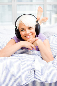 听音乐用耳机在床上的金发女郎
