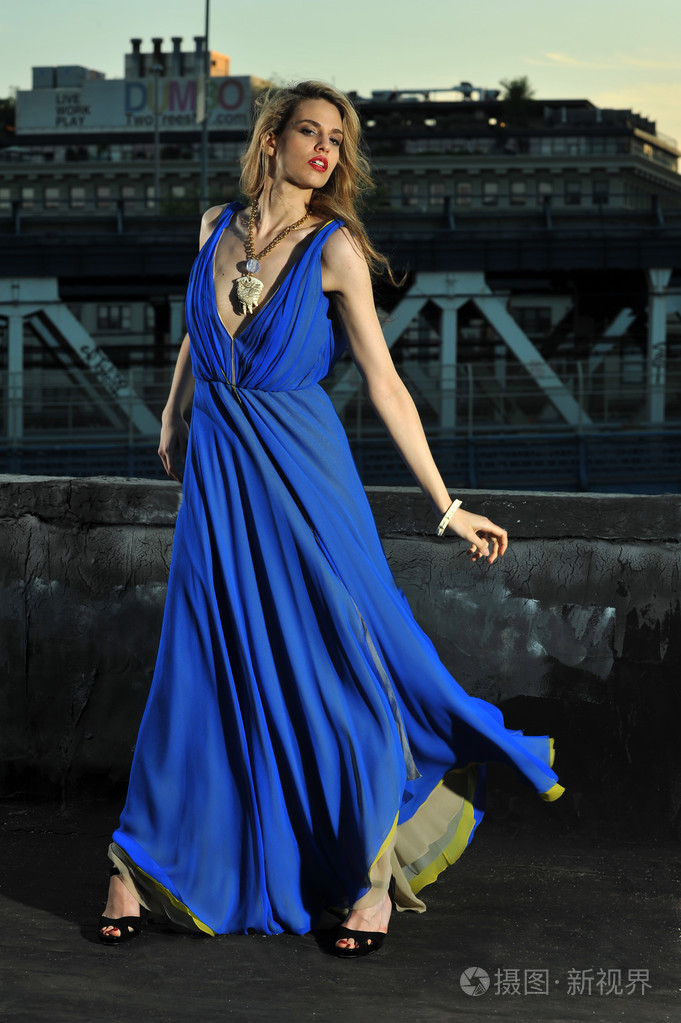 时装模特姿势性感穿长袖蓝色晚礼服的屋顶位置上背景上金属桥梁施工