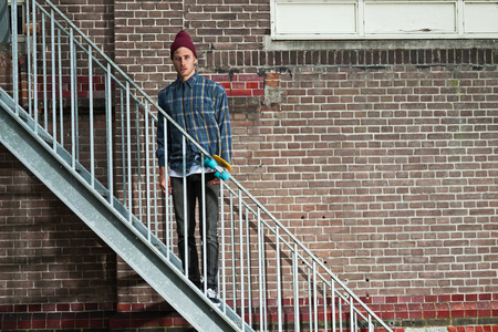 与羊毛帽子站在铁楼梯上的酷滑板手。他