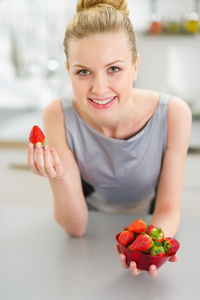 快乐年轻家庭主妇在厨房里吃草莓