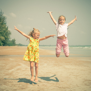 飞跳海滩在蓝色海洋上的两个女孩在暑假期间岸