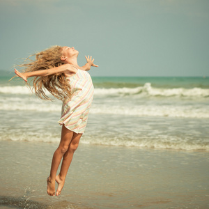 飞行在暑假期间在蓝色的大海岸上跳沙滩女孩