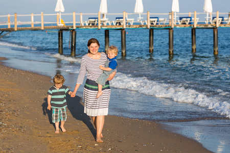 幸福的母亲和两个孩子在沙滩上散步