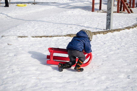 蓝色外套的男孩跪下去红色雪橇