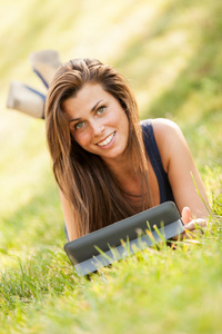 在草地上的漂亮黑发女孩正在看一个数字屏幕