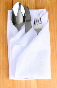折的餐巾与叉子 勺子和木制背景上刀