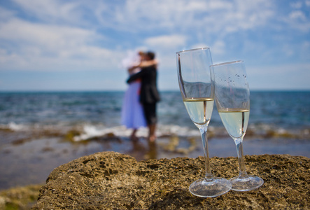 主题婚礼新娘和新郎手牵着手，在前景香槟眼镜的海上