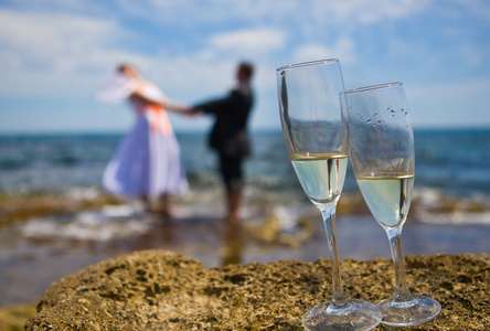 主题婚礼新娘和新郎手牵着手，在前景香槟眼镜的海上