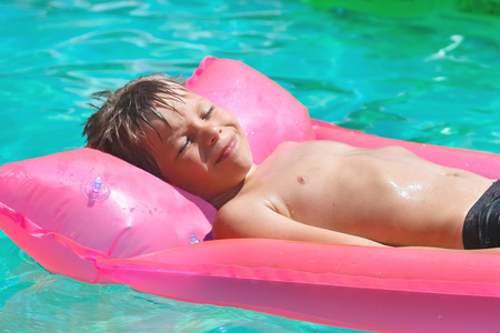 微笑的男孩躺在池中的粉红色床垫