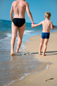 年轻爸爸和小儿子在海洋海滩散步