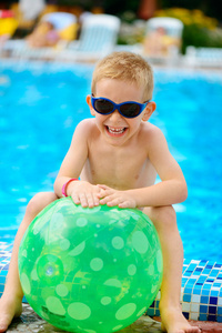 可爱的男孩坐在游泳池旁的墨镜
