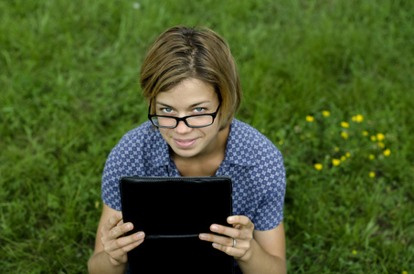 年轻女子在眼镜中使用一个数字平板在草地上