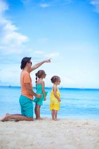 快乐的父亲与他两个女儿坐在热带海滩度假